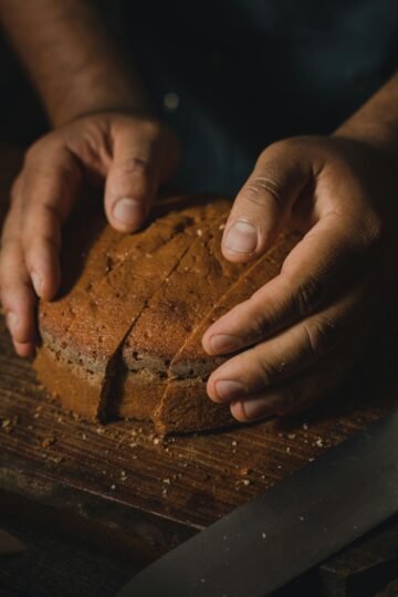 Hands gently holding a loaf of artisan bread on a wooden board in a cozy, rustic setting.