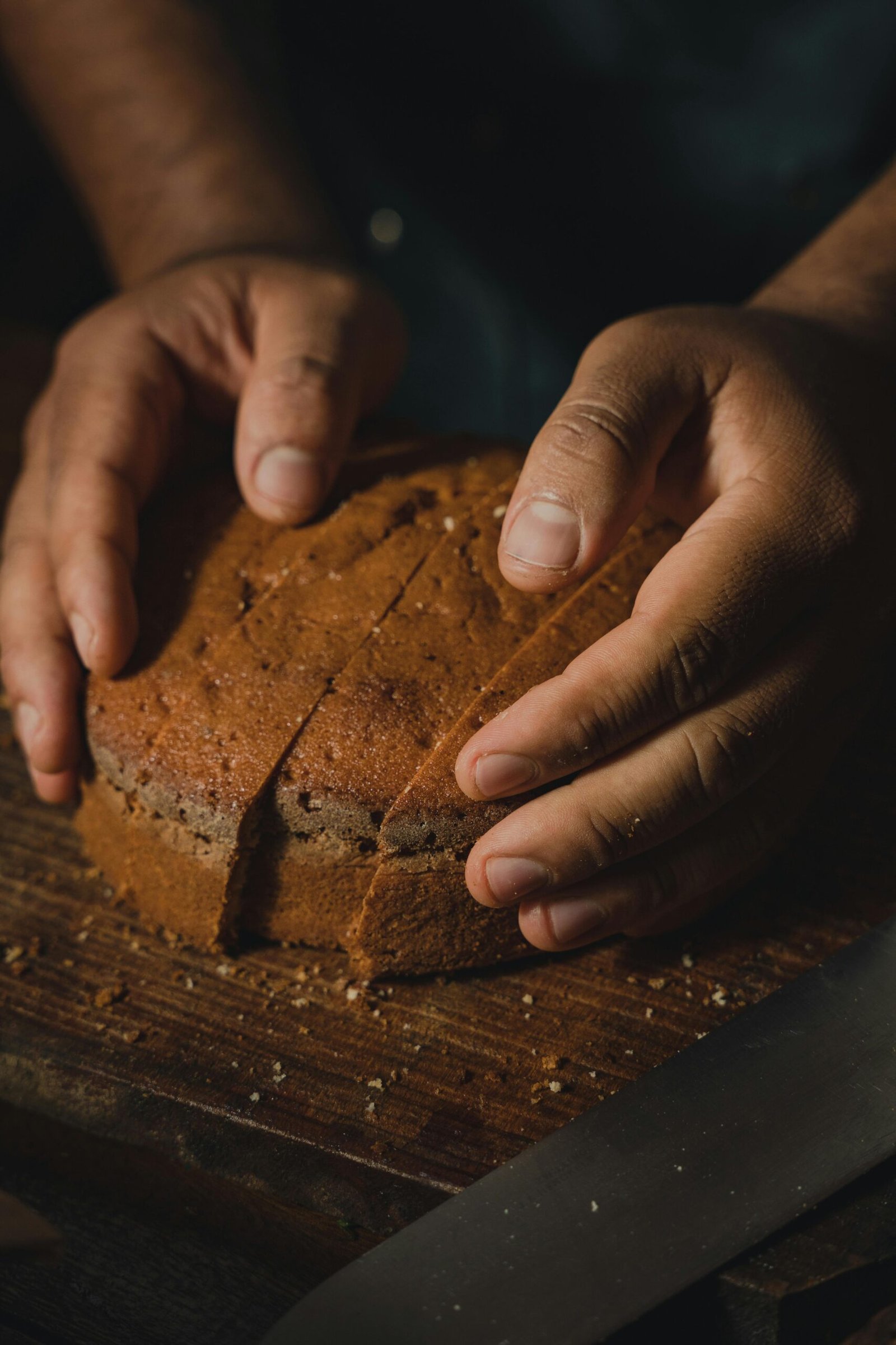 Hands gently holding a loaf of artisan bread on a wooden board in a cozy, rustic setting.