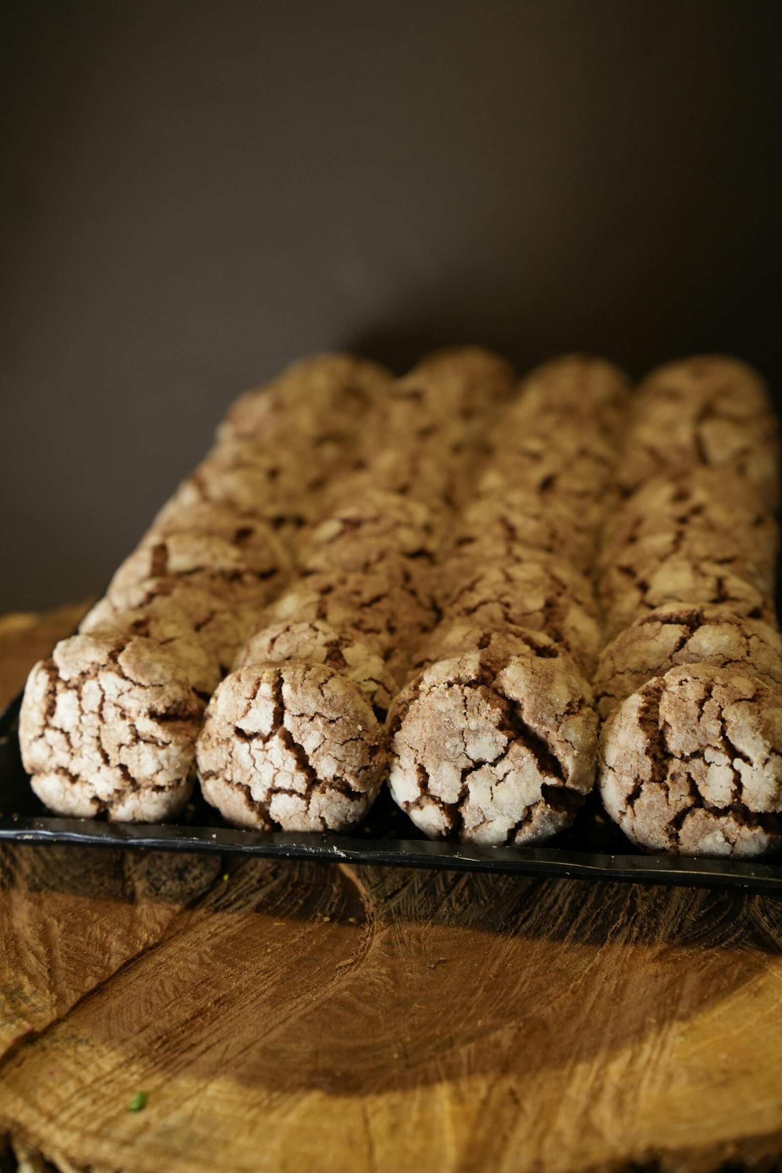 Row of freshly baked crackled chocolate cookies on a wooden slab.