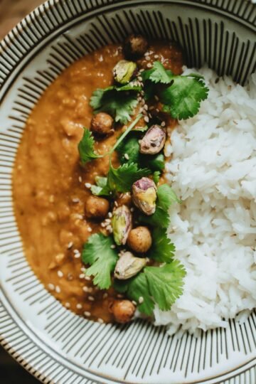 Delicious vegan rice bowl featuring lentil curry, topped with pistachios, cilantro, and sesame seeds.